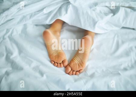 Girl's feet covered with white bed sheet, sleeping in a comfortable bed ...