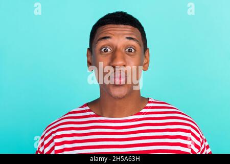 Photo of excited funny young guy dressed red t-shirt sending you kiss isolated turquoise color background. Stock Photo