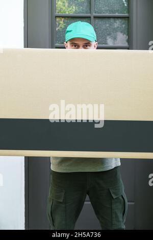 A large cardboard box in the hands of a courier standing at the door of the house. Delivery package to the address. Stock Photo