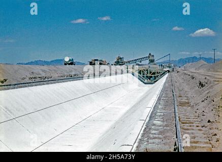 Construction work on the Wellton-Mohawk canal, near Yuma, Arizona, USA in the early 1950s. The canal lining machine works its way along the canal’s profile. The giant mechanical device on rails lays concrete, poured from the hopper at its top, which will form the base and sloping sides of the waterway. The Wellton-Mohawk Irrigation and Drainage District is located in south-west Arizona, east of Yuma, built between 1949 and 1957. It allows the irrigation in the Lower Gila valley with water from the Colorado river via the Gila Canal to the Wellton-Mohawk Canal, where it is pumped around 160 feet Stock Photo