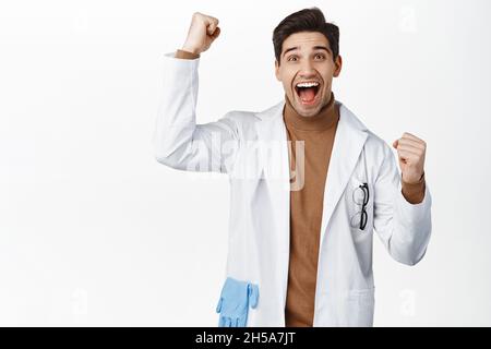 Enthusiastic medical worker, doctor in robe cheering, shouting from joy, winning, standing over white background Stock Photo