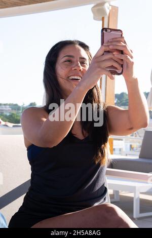 Latin woman sitting on a terrace talking on a video call with a friend. Stock Photo
