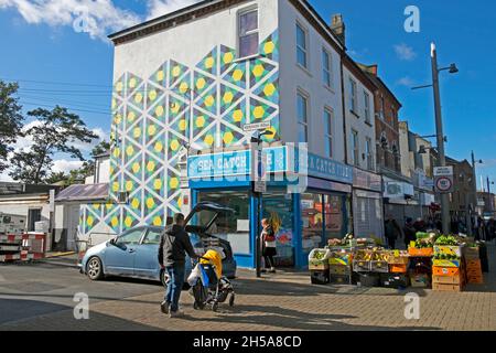 Walthamstow High Street geometrical wall painting on building, shops,  fruit veg market stall in autumn sunshine October 2021 London UK KATHY DEWITT Stock Photo
