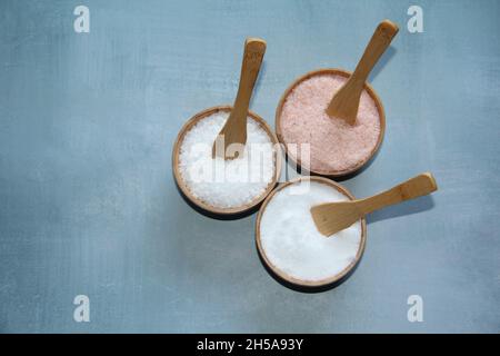 Himalayan pink salt, fine salt and coarse salt in crystal stones in wooden bowls on a light blue background, top view. Stock Photo