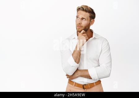 Portrait of stylish and handsome blond man looking aside, thinking, making decision, standing thoughtful over white background Stock Photo