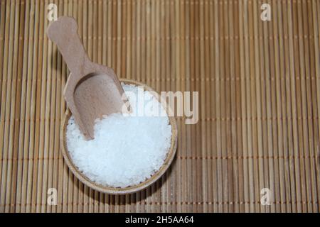 Coarse salt, in a wooden bowl, with a measuring spoon, on a bamboo mat. View from above. Stock Photo