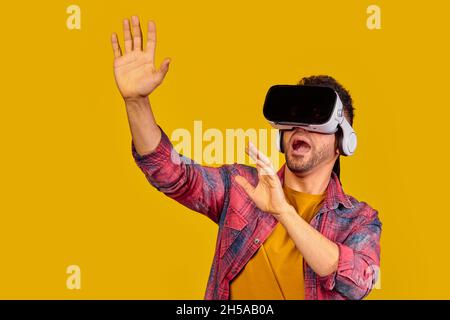 Surprised young guy in VR glasses on a yellow background, man use virtual reality glasses, copy space. High quality photo Stock Photo