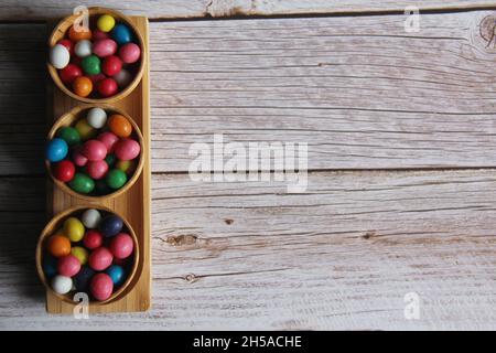 Peanut candies with colored sugar icing, in three wooden bowls on an old wooden table. Stock Photo