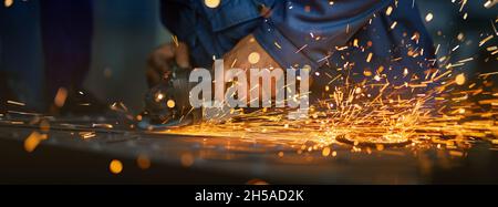 Close up of male hands using special tool for cutting metal at workshop. Sparks flying from metal processing. Craft production.  Stock Photo