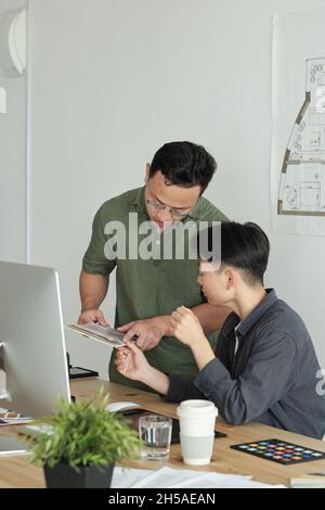 Two young designers of Asian ethnicity discussing color samples for new project at working meeting in office Stock Photo