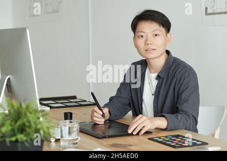 Pretty young Asian designer drawing sketch on computer screen while working over new architectural project in office Stock Photo