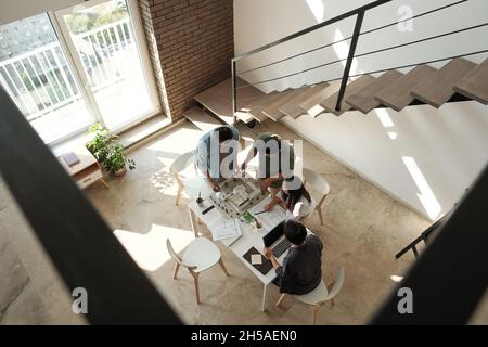 Four young Chinese architects discussing layout of new city district while standing by table in large office Stock Photo