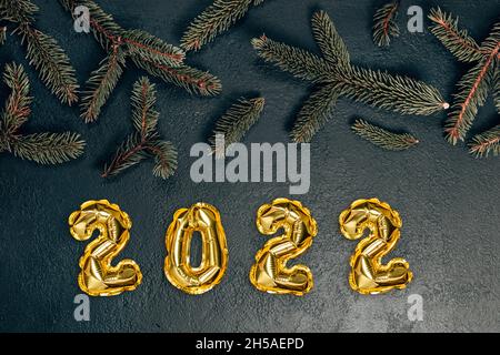 Creative Christmas background with green fir branches and 2022 text golden foil balloons decor. Stock Photo