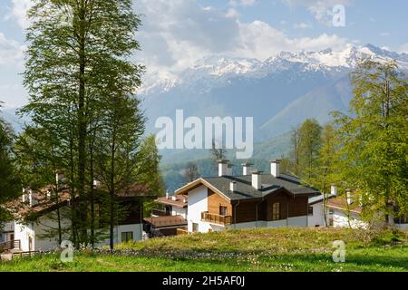 Sochi Krasnodar Territory village of Rosa Khutor on April 29, 2018. View of wooden guest houses and mountains. Beautiful sunny spring landscape at a p Stock Photo