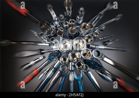 Various tools (wrenches, heads, ratchets, extension cords, bits) arranged in star on a dark background with a radial blur effect Stock Photo