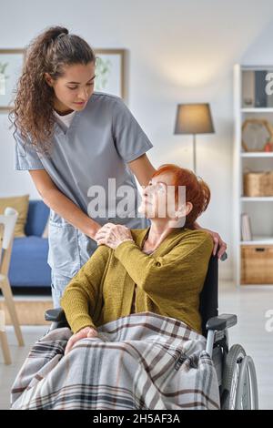 Young nurse talking to senior woman who using wheelchair, she caring about her in nursing home Stock Photo