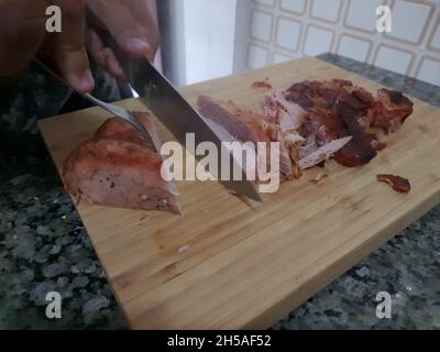 Male hands slicing a roast pork loin on a wooden board. Stock Photo
