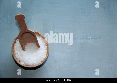 Coarse salt, in a wooden bowl, with a wooden measuring spoon on an old wooden table. View from above. Stock Photo