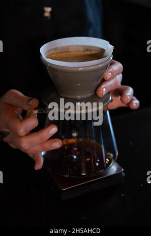 barista pour hot water on rough brown bubbles coffee through drip filter, home brewing process. preparing coffee using chemex pour over coffee maker a Stock Photo