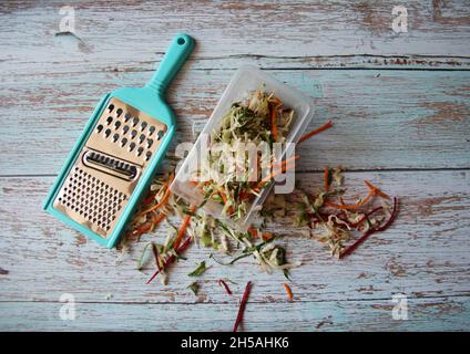Vegetables and vegetables: carrots, cabbage, beets, grated, in a bowl with a grater on an old wooden table. View from above. Space for text. Stock Photo
