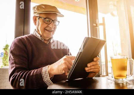 Senior man is sitting in cafe and using digital tablet. Stock Photo
