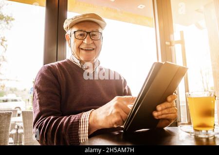 Senior man is sitting in cafe and using digital tablet. Stock Photo