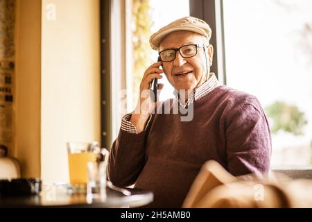 Senior man is sitting in cafe and talking on phone. Stock Photo