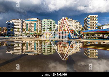 high rise flats and funfair of Vlora Albania are reflected in rainwater as another storm approaches Stock Photo