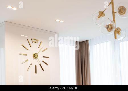 A huge clock in gold color on the wall in a modern beige interior. Interior Design. Soft selective focus, artistic noise. Stock Photo