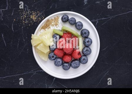 White plate with fresh berries and fruits on black marble Stock Photo