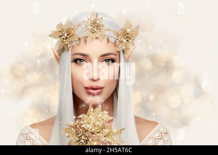 Elf queen with golden flowers wreath looking at camera blowing magic ...