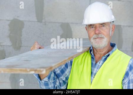 senior worker wearing hard hat and carrying timber Stock Photo