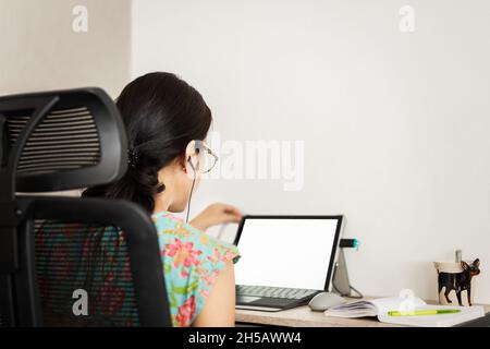 Back view of woman in earphones making video call on laptop. Stock Photo