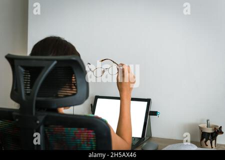 Asian businesswoman holding eyeglasses while working overtime on laptop at home. Stock Photo