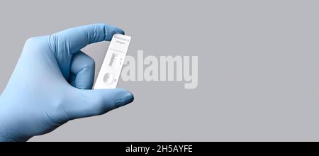 Gloved hand holding a positive rapid test device for COVID-19. Panoramic image with copy space. Stock Photo