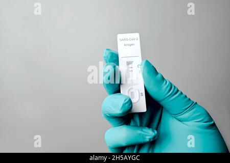 Gloved hand holding a positive rapid test device for COVID-19. Isolated on gray background. Stock Photo