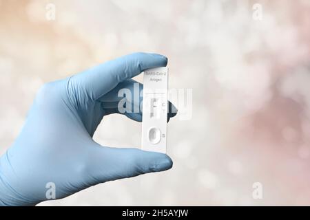 Gloved hand holding a negative rapid test device for COVID-19 in front of bokeh background. Stock Photo
