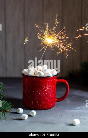 Red mug of christmas coffee or cocoa with marshmallows and sparklers on grey stone table. Xmas holiday concept Stock Photo