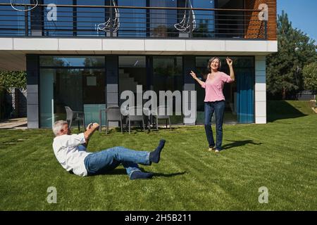 Aging man lying on grass taking picture of his wife Stock Photo