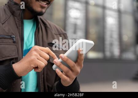 Closeup of Indian man holding mobile phone texting message standing outdoors Stock Photo