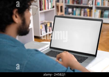 Indian teen male student working with laptop white screen mockup at library Stock Photo
