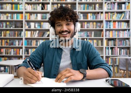 Portrait of smiling Indian student in headset looking at camera at library desk Stock Photo