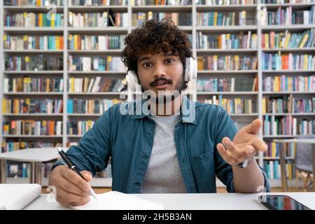 Young Indian male student wearing headset talking to camera sitting in library Stock Photo