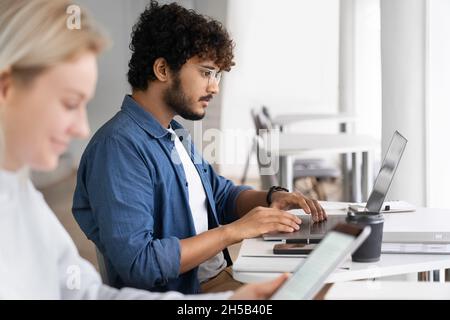 Male and female student sitting at desk table studying using digital gadget Stock Photo