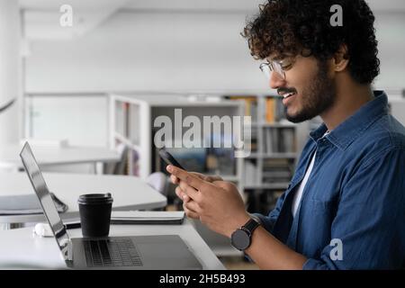 Young Indian man open social media using smartphone sitting front of computer Stock Photo
