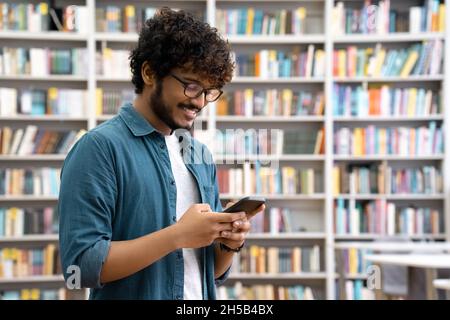 Side view portrait of happy young Indian student chatting by phone in library Stock Photo