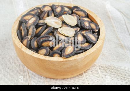 Black dry watermelon seeds in wooden bowl on the tablecloth. Stock Photo