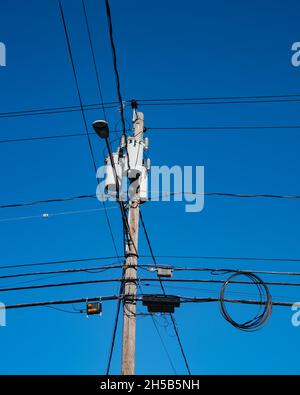 A utility pole with transformers, a street light, junction boxes and wires and cables with a deep blue sky background. Stock Photo