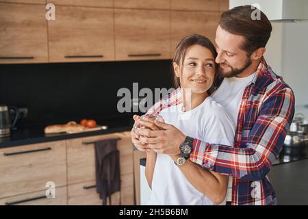 Handsome Caucasian man hugging his girlfriend in the kitchen Stock Photo