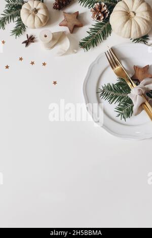 Festive Christmas table setting. Golden cutlery, spruce tree branch. White pumpkins isolated on white background. Pine cones, confetti stars Stock Photo